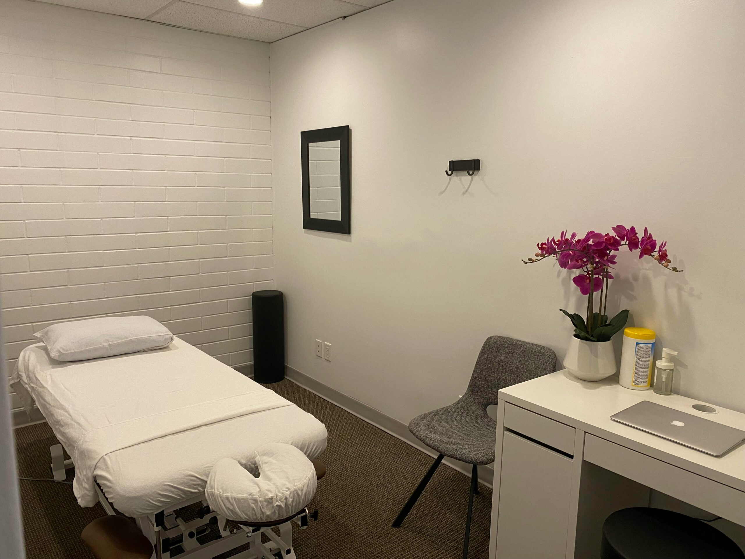Spa treatment room at Aura Health & Spa featuring a massage table, decorative orchids, and a modern aesthetic, highlighting relaxation and wellness ambiance.